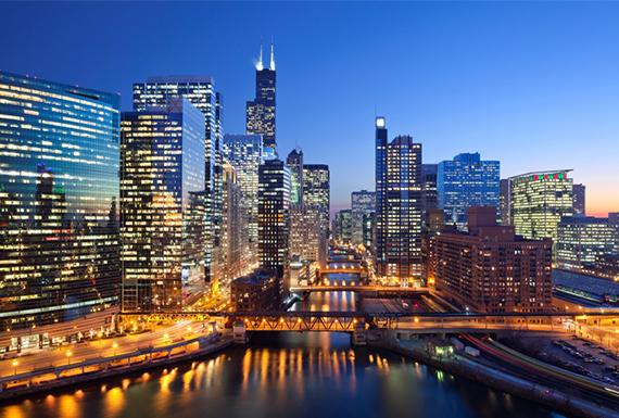 Chicago River reflecting the city skyline at dusk, with buildings illuminated against a twilight sky.